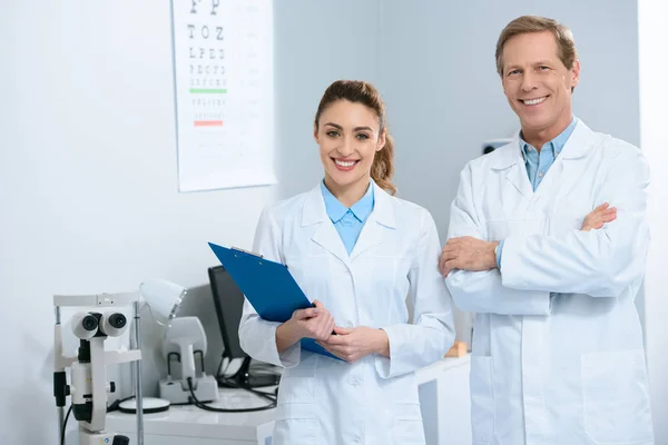 Oftalmólogos sonrientes de pie con diagnóstico en la clínica - foto de stock
