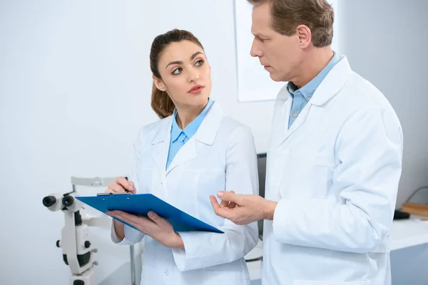 Male and female ophthalmologists writing diagnosis in clinic — Stock Photo