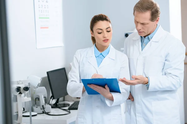 Male and female optometrists writing diagnosis in clinic — Stock Photo
