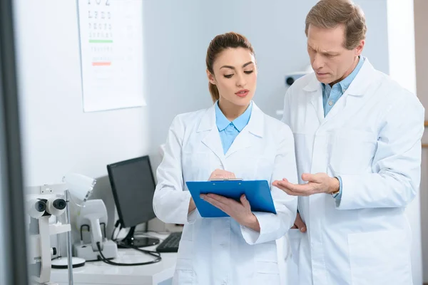 Optometristas masculinos y femeninos que escriben diagnóstico en clínica - foto de stock