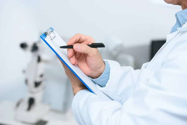 Ausgeschnittene Ansicht eines Optikers, der Diagnose in Klinik schreibt — Stockfoto