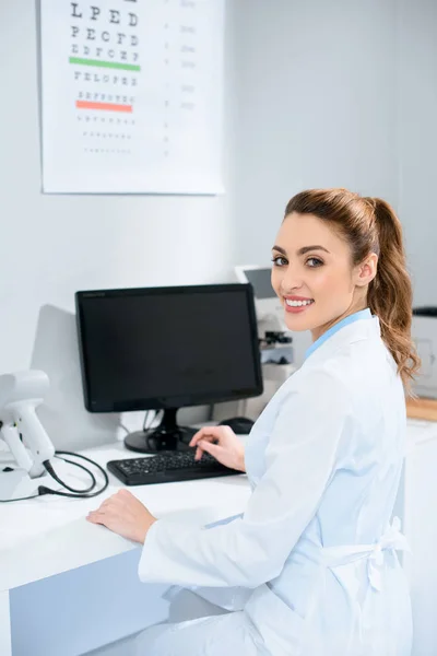 Opticien femme souriante travaillant avec l'ordinateur dans la clinique — Photo de stock
