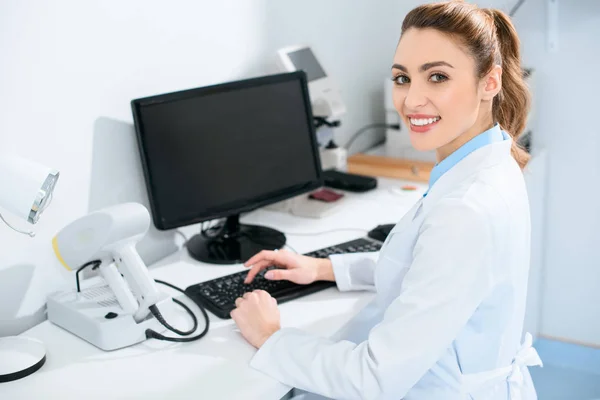 Atractiva oftalmóloga femenina que trabaja con computadora en la clínica - foto de stock