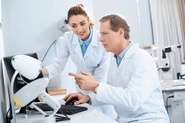 Dos ópticos trabajando con el ordenador en la clínica - foto de stock