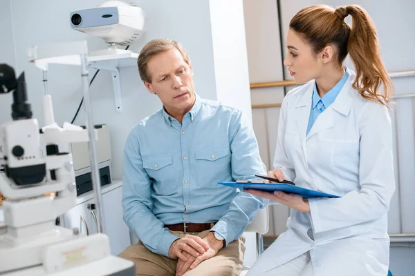 Oculist writing diagnosis after examination of middle aged man — Stock Photo