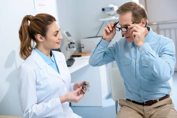 Optometrista y hombre maduro eligiendo gafas en óptica - foto de stock