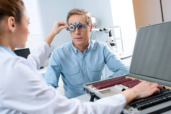 Female ophthalmologist examining middle aged man eyes with trial frame — Stock Photo