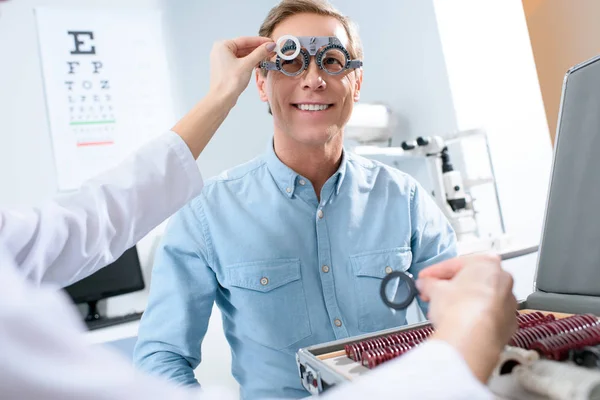 Ophtalmologiste examinant les yeux d'homme d'âge moyen avec monture d'essai et lentilles — Photo de stock