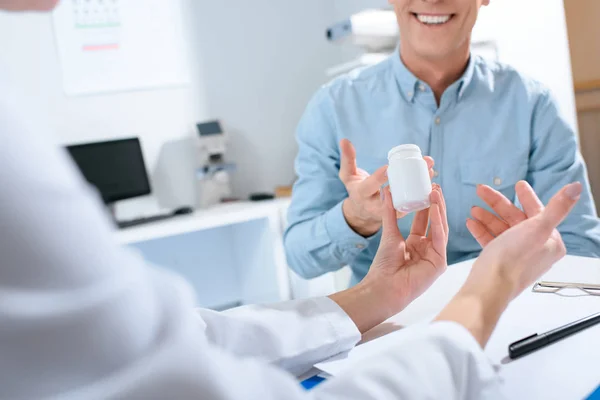 Cropped view of doctor holding bottle of pills and talking with patient in clinic — Stock Photo