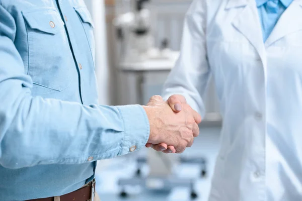 Visão parcial do homem apertando as mãos com o médico na clínica — Fotografia de Stock