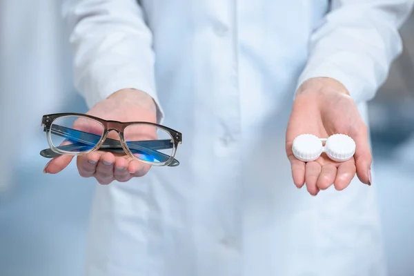 Cropped view of ophthalmologist holding eyeglasses and and contact lenses in hands — Stock Photo