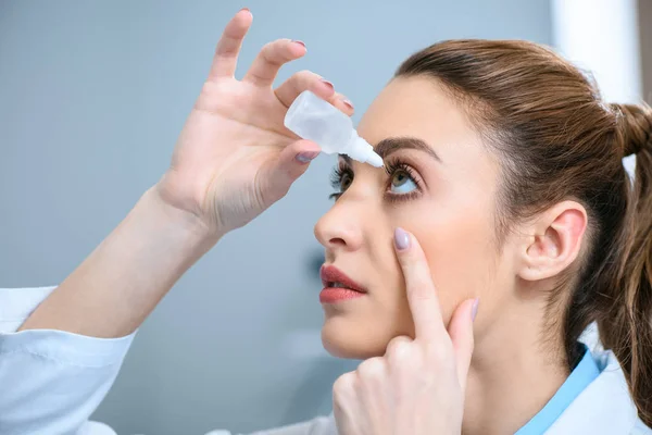 Mujer optometrista goteo gotas para los ojos - foto de stock