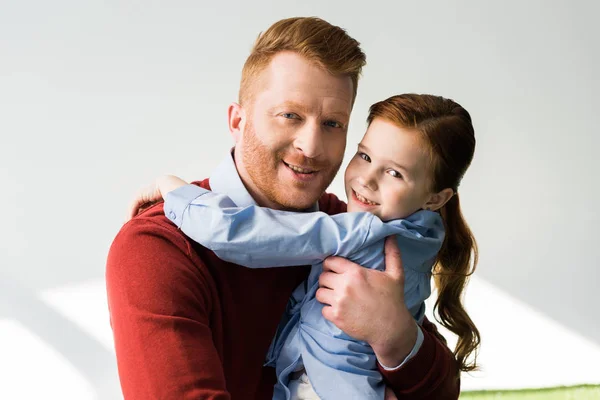 Happy redhead father and daughter hugging and smiling at camera on grey — Stock Photo