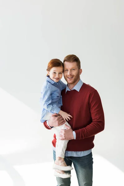Felice padre portando adorabile figlioletta e sorridendo alla macchina fotografica su grigio — Foto stock