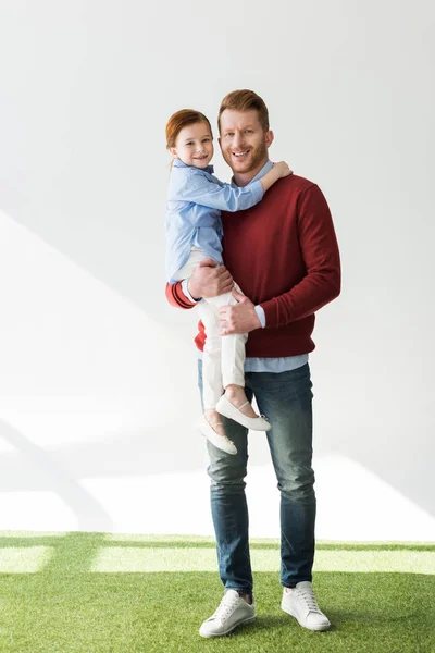 Щасливий батько носить чарівну маленьку доньку і посміхається на камеру на сірому — стокове фото