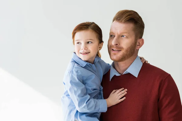 Feliz pelirroja padre e hija abrazando y mirando hacia otro lado en gris - foto de stock