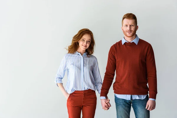 Happy redhead couple holding hands and smiling at camera isolated on grey — Stock Photo