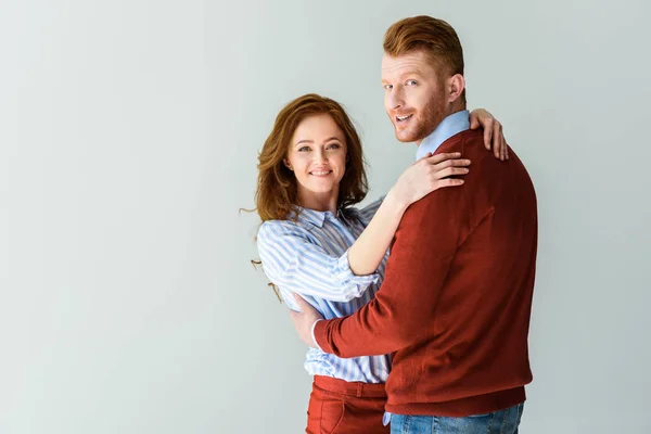 Beautiful happy red haired couple hugging and smiling at camera isolated on grey — Stock Photo