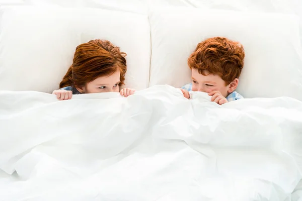 Top view of cute little redhead children hiding under blanket and looking at each other — Stock Photo