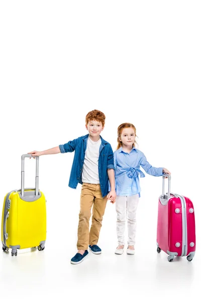 Cute redhead children holding hands while standing with suitcases isolated on white — Stock Photo