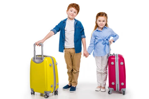 Cute little kids holding hands while standing with suitcases and smiling at camera isolated on white — Stock Photo