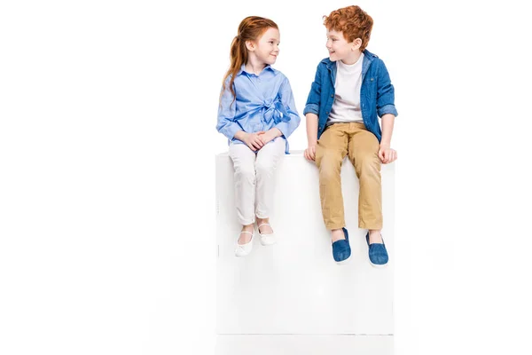 Adorables niños pequeños sentados en cubo blanco y sonriéndose aislados en blanco - foto de stock