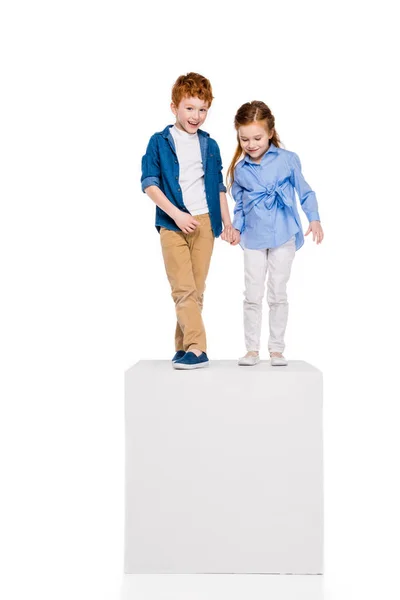 Adorable little kids holding hands and standing on white cube isolated on white — Stock Photo