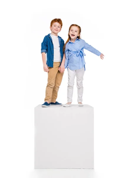 Lindo feliz niños de pie en blanco cubo y sonriendo a la cámara aislado en blanco - foto de stock