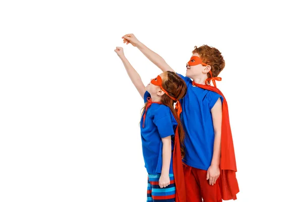 Super niños con máscaras y capas levantando las manos y mirando hacia otro lado aislado en blanco - foto de stock