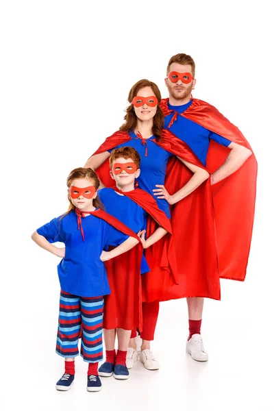 Super familia en máscaras y capas de pie con las manos en la cintura y sonriendo a la cámara aislada en blanco - foto de stock