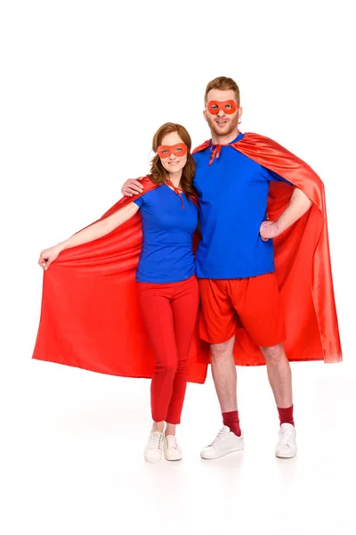 Super couple in masks and cloaks standing together and smiling at camera isolated on white — Stock Photo