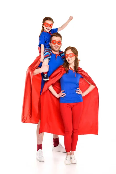 Super familia con un niño en máscaras y capas sonriendo a la cámara aislada en blanco - foto de stock