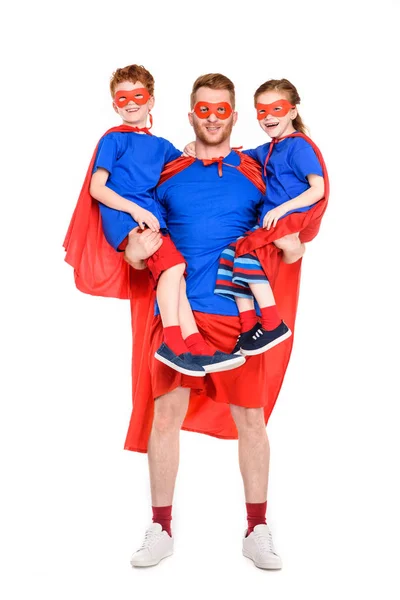 Super padre llevando niños felices en máscaras y capas aisladas en blanco - foto de stock