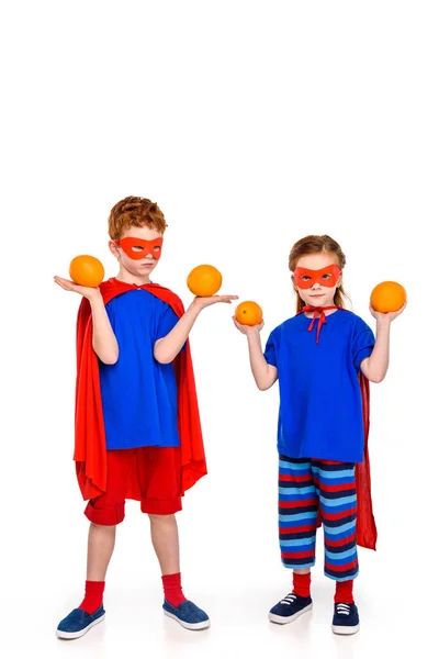 Adorable little kids in superhero costumes holding oranges isolated on white — Stock Photo