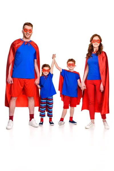 Vista completa de la feliz super familia en máscaras y capas cogidas de la mano y mirando a la cámara aislada en blanco - foto de stock
