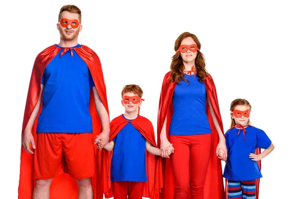 Super familia en máscaras y capas cogidas de la mano y mirando a la cámara aislada en blanco - foto de stock