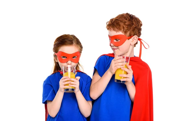 Adorable little children in superhero costumes drinking juice isolated on white — Stock Photo