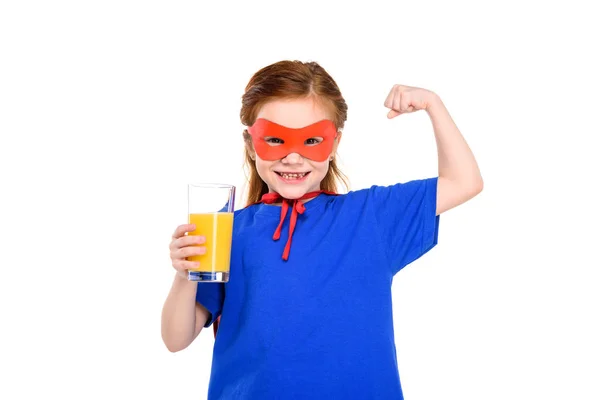 Happy child in superhero costume holding glass of juice and showing biceps isolated on white — Stock Photo