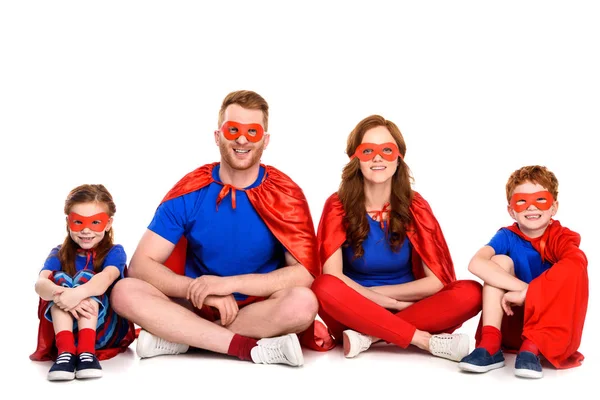 Familia feliz de superhéroes sentados juntos y sonriendo a la cámara aislada en blanco - foto de stock