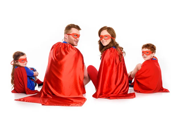 Back view of family of superheroes sitting together and looking at camera isolated on white — Stock Photo