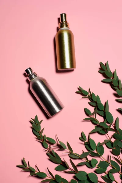 Top view of metal bottles of perfumes with green branches on pink surface — Stock Photo