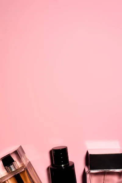 Vista superior de botellas de varios perfumes en la superficie de color rosa en blanco - foto de stock