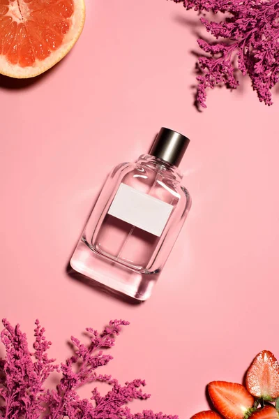 Draufsicht auf eine Flasche Parfüm mit rosa Blüten, Orange und Erdbeere auf rosa Oberfläche — Stockfoto