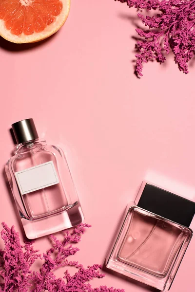 Vista dall'alto di bottiglie di profumi con fiori rosa e arancione sulla superficie rosa — Foto stock