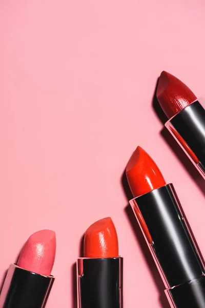Draufsicht auf verschiedene Lippenstifte mit roten Farbtönen auf rosa Oberfläche — Stockfoto