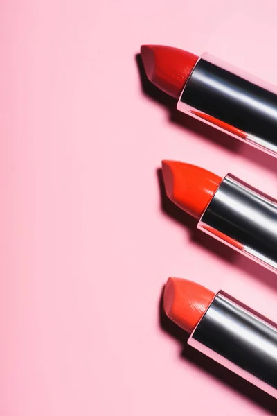Draufsicht auf verschiedene Lippenstifte roter Farbtöne in Reihe auf rosa Oberfläche — Stockfoto