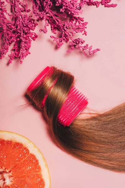 Vue de dessus des cheveux roulés sur curler avec des fleurs et orange sur la surface rose — Photo de stock
