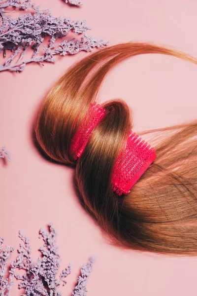 Vue de dessus des cheveux roulés sur le bigoudis avec des fleurs sur la surface rose — Photo de stock