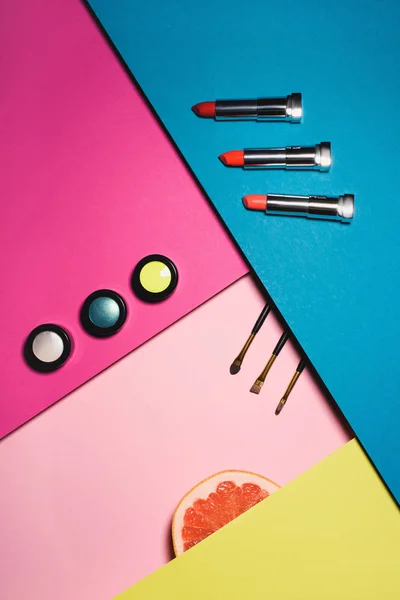 Vista superior de varios suministros de maquillaje con rodaja de pomelo en superficies coloridas - foto de stock