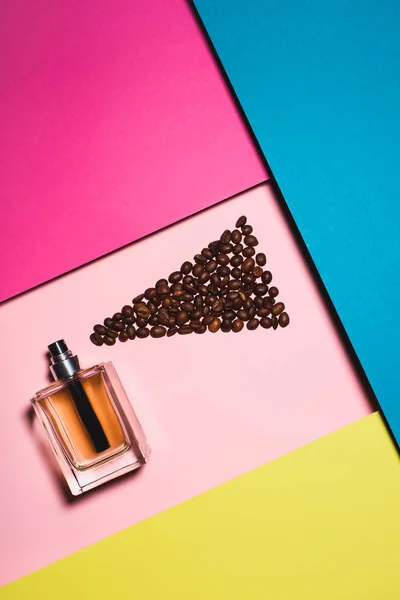 Vue de dessus de bouteille en verre de parfum avec des grains de café sur une surface colorée — Photo de stock